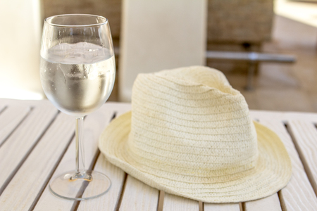 white hat and glass with water and ice on a white wooden table on a sunny summer dayの写真素材