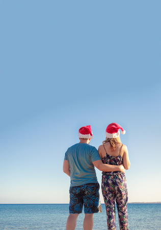 man hugging woman in christmas hats and looking at the beach of the sea.の写真素材