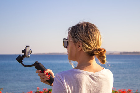 Attractive female records video with modern 3d gimbal stabilized camera smartphone
