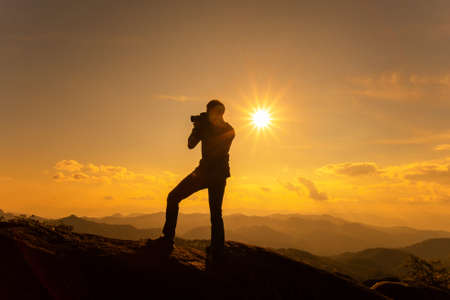 Silhouette of a photographer taking photo of beautiful landscape on the high mountain during sunset moment.の写真素材