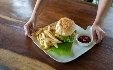 Hands holding a hamburger, Young girl holding fast food burger with french fries, tomato sauce on a...