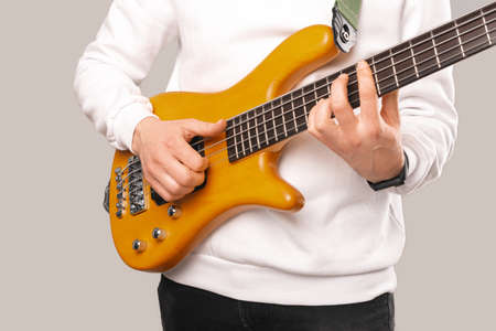 Faceless photo of a man wearing white and playing and practicing bass guitar Studio shot over grey...