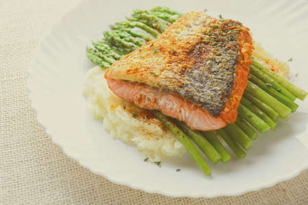 Grilled salmon garnished with asparagus and herbs and mashed potatoes, served on white plated.