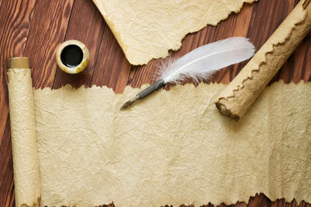 Closeup of scroll and quill near ink-pot on wooden table