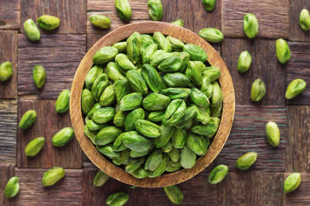 pistachios nuts peeled green in bowl on wooden table background.