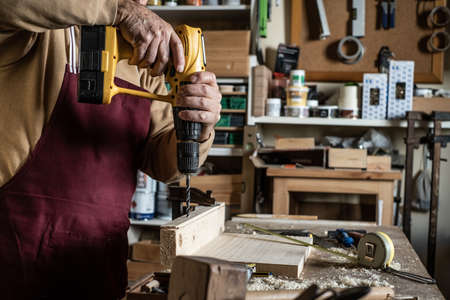 Carpenter with a yellow drill making a hole with a wooden drill on boardの写真素材