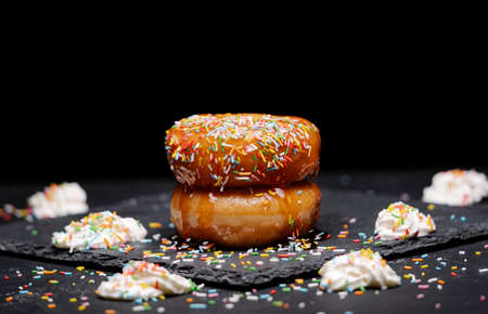 donuts with strawberry syrup and coloured topping with cream on a black backgroundの写真素材