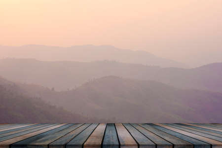 Wooden table and blur of beauty, sunset sky, and mountains as background.の写真素材