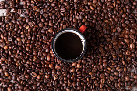 Coffee beans background with a red cup in the center with freshly made coffeeの写真素材