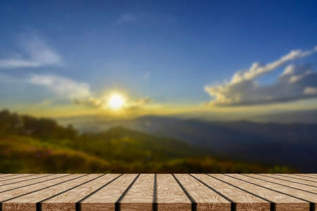 Wooden table and blur of beauty, sunset sky, and mountains as background.の写真素材