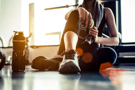 Sport woman sitting and resting after workout or exercise in fitness gym with protein shake or drinking water on floor. Relax concept. Strength training and Body build up theme. Warm and cool toneの写真素材