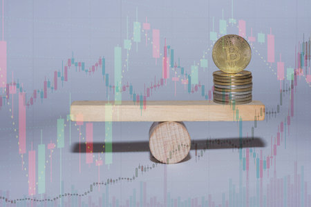 stacked bitcoin on a wooden seesaw with charts from the market on gray backgroundの写真素材