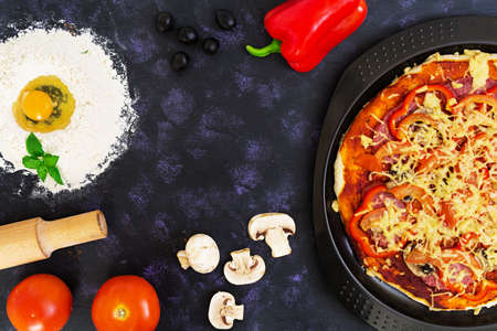 Raw pizza dough with ingredients and spices on dark background. Top viewの写真素材
