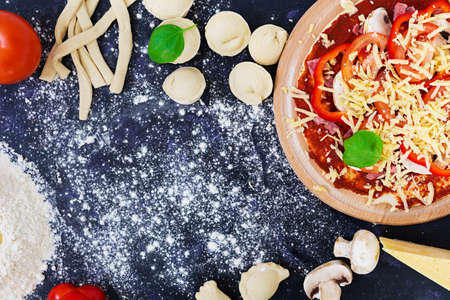 Raw pizza dough with ingredients and spices on dark background. Top viewの写真素材