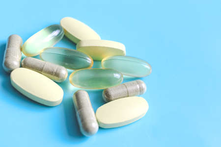 Amber color gel medicine capsules and yellow supplement nutrient pills on blue background,...