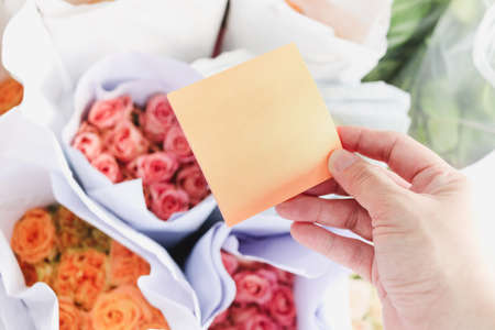 Blank note paper in hand on beautiful rose flower bouquet background, copy-space on card to put your...