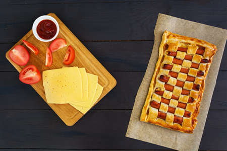 Sausage pie in puff pastry on dark background
