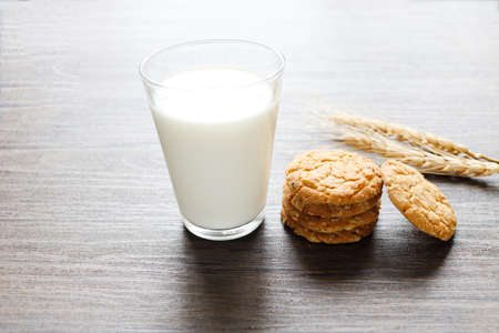 Delicious oatmeal cookies with spikelets and glass of milk on wooden table.の写真素材