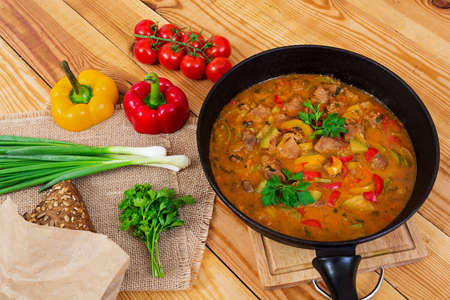 Stew with meat and vegetables in tomato sauce on wooden background