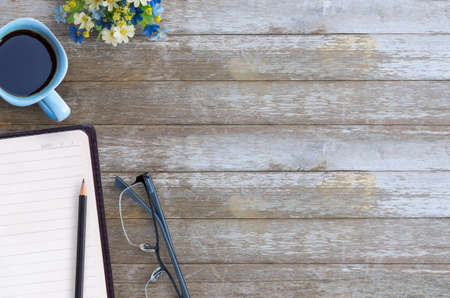 Blank paper notebook,glasses,pencil and cup of coffee on brown wooden table background. Top view with copy space (selective focus). Office desk table concept.の写真素材