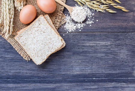 Ears of wheat and egg with slice of bread on a dark wooden table background