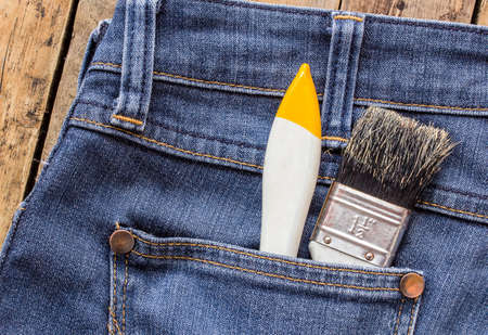 Two paint brushes in jeans pocket on wooden tableの写真素材