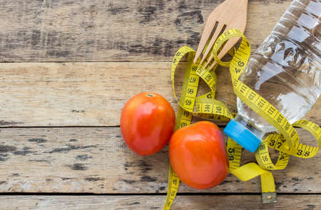Yellow measuring tape, tometos and bottle water on wooden table - fitness conceptの写真素材
