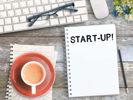 Top view with start up on notebook,keyboard,coffee and glasses on wood table in office workplace. Business and education concept ideas.の写真素材