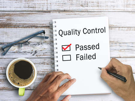 Handwriting Quality Control Form. The box with Passed is checked in red on notebook,keyboard,coffee and glasses on wood table in office workplace. Business and education concept ideas.の写真素材