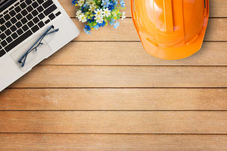 Office desk table with orange safety helmet,laptop computer,glasses on wooden table background.