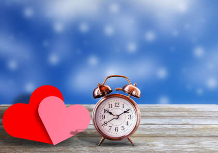 Red and pink heart and vintage alarm clock on wood panel table with bokeh light as background. copy space for design. Love and valentines day concept.の写真素材