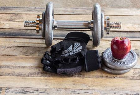 Red apple and dumbbells, extra weights and black gloves on the wooden floorの写真素材