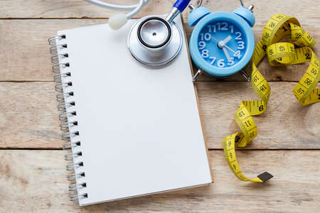 Healthy lifestyle concept with apples. Weight loss or diet concept. Blue stethoscope,alarm clock and yellow measure tape with note pad on wood table background with copy space for designの写真素材