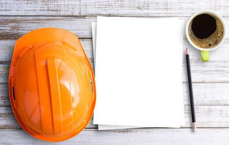 Top view Safety Engineer Helmet,cup of coffee,pencil and blank paper on brown wooden table...
