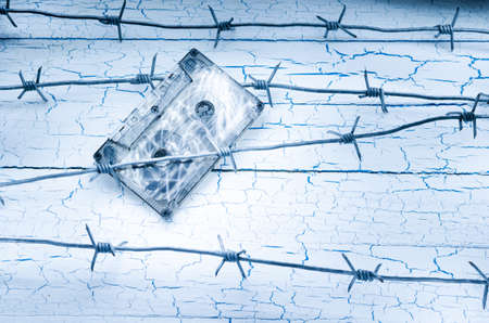 Audio cassette tape hanging on the barbed wire on the background of the old wallの写真素材