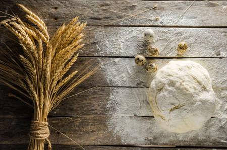 Ears of wheat kneaded dough and quail eggs on old wooden table