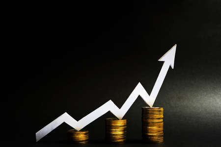 Stacks of coins with a white arrow growing up. Concept of growth and increase in income and economy on a black backgroundの写真素材