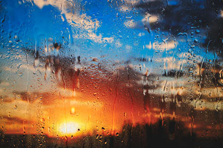 Bright summer sunset behind dripping glass after rainの写真素材