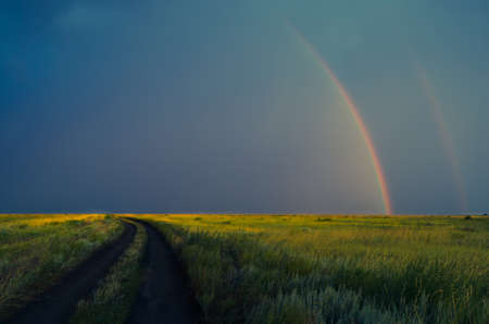 Double rainbow after rain on the background of storm clouds.Road in the field in the evening.の写真素材