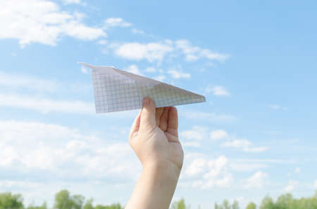 Hand of little boy runs paper airplane in the sky.On bright Sunny day.