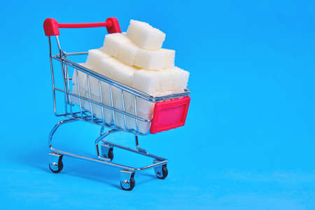 Shopping cart is filled with refined sugar cubes on a blue backgroundの写真素材