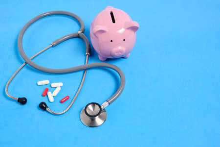Stethoscope, bunch of pills and piggy bank on blue backgroundの写真素材