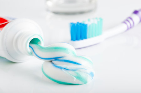 Toothbrush, tube of toothpaste and a glass on a white background
