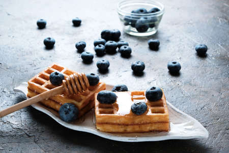 Waffles are laid out on plate, decorated with blueberries, doused with honey from honey spoonの写真素材