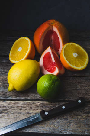 Tinted vertical photo of citrus fruits orange grapefruit lemon and lime on the old wooden table with knifeの写真素材