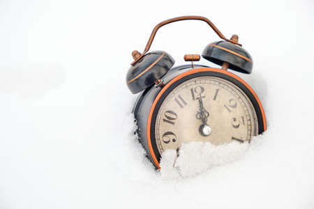Old retro alarm clock in winter in snow on white background shows twelve hoursの写真素材