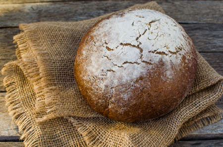 Loaf of black bread on old wooden table, the rays of the morning sun