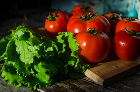 Ripe tomatoes on a cutting Board and salad leaves on old tableの写真素材