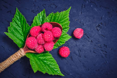 Raspberry berry in a wooden spoon and a green raspberry leaf on a dark background