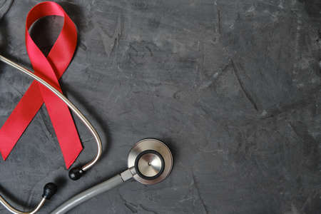 Red ribbon symbol of AIDS, drug abuse problem, stethoscope on concrete texture backgroundの写真素材